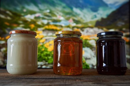 Various honey types in jars on a wooden board in a beautiful mountain view with flowers