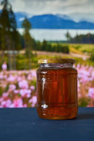 Téléchargez les photos : Miel en pots sur planche en bois dans une belle vue sur la montagne avec des fleurs - en image libre de droit