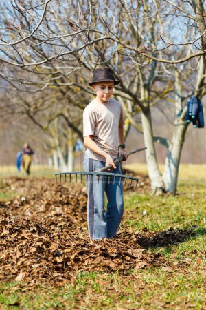 Photo for Kid with his grandmother and his mother spring cleaning with a rake in an orchard - Royalty Free Image