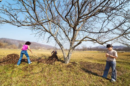 Photo for Family spring cleaning with rake in an orchard - Royalty Free Image