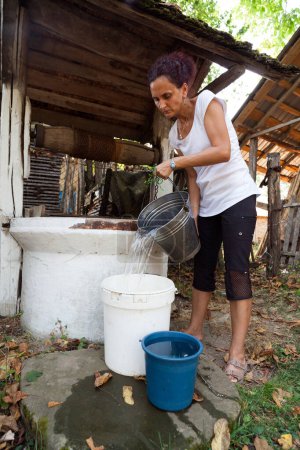 Téléchargez les photos : Portrait d'une jeune femme recevant de l'eau d'un puits en bois vintage - en image libre de droit