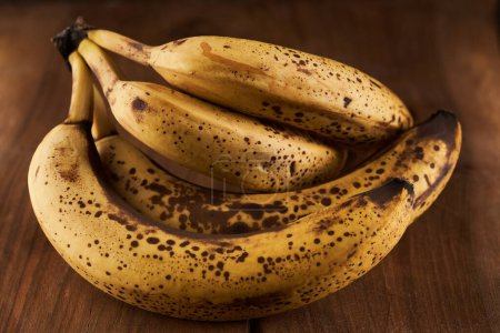 Foto de Manojo de plátanos dulces demasiado maduros en una tabla de madera rústica - Imagen libre de derechos