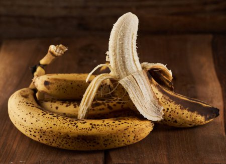 Foto de Manojo de plátanos dulces demasiado maduros en una tabla de madera rústica - Imagen libre de derechos