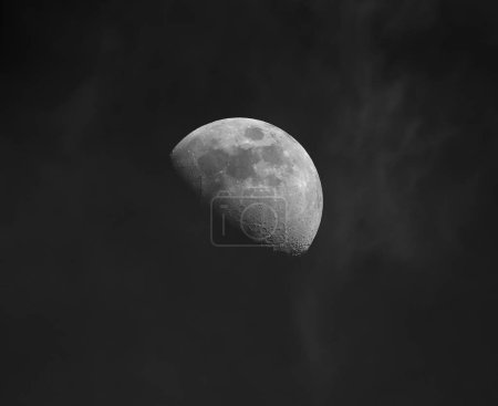 Téléchargez les photos : Vue de la Lune demi-phase avec cratères et détails, sur un ciel sombre avec des nuages ondulés - en image libre de droit
