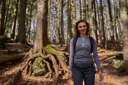 Téléchargez les photos : Femme avec sac à dos randonnée seule sur un sentier dans les montagnes, à travers la forêt - en image libre de droit