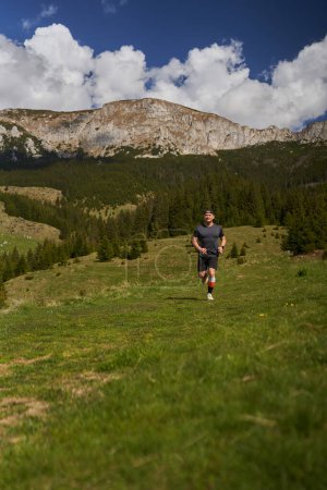 Foto de Corredor de senderos en una carrera con montañas detrás en un prado - Imagen libre de derechos