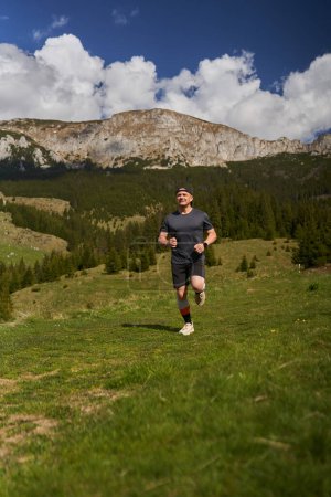 Foto de Corredor de senderos en una carrera con montañas detrás en un prado - Imagen libre de derechos