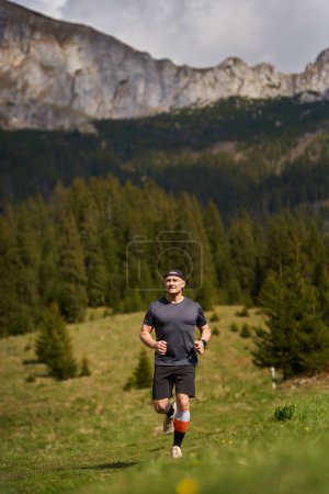 Photo for Trail runner in a race running with mountains behind on a meadow - Royalty Free Image
