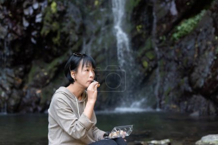 Foto de Mujer asiática comer sushi cerca de la cascada al aire libre - Imagen libre de derechos
