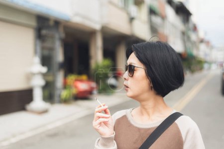 Photo for Modern Asian beauty with glasses smoking at street in the city - Royalty Free Image