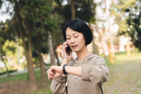 Photo for Asian woman talk on cellphone and using smart watch - Royalty Free Image
