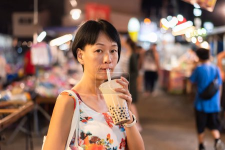 Foto de Mujer asiática sosteniendo el famoso té de leche de burbuja taiwanés en el mercado nocturno - Imagen libre de derechos