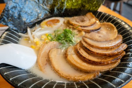 Pork belly slices atop ramen in a rich broth, garnished with egg and vegetables.