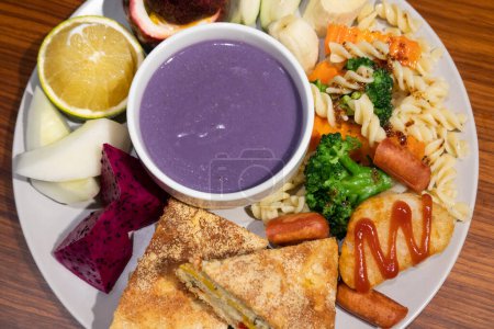 Téléchargez les photos : Assiette copieux petit déjeuner avec œufs, saucisses, fruits et soupe violette. - en image libre de droit