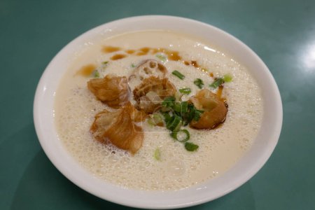 Bowl of savory soy milk soup with youtiao (fried dough sticks) and scallions.