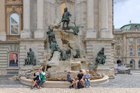 Foto de Budapest, Hungría - 31 de julio de 2022: Turistas sentados frente a estatuas de bronce cazando la Fuente Motiva del Rey Matías en el Castillo de Buda. - Imagen libre de derechos