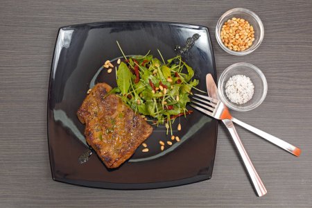 Foto de Ensalada de bistec a la parrilla y rúcula con nueces de pignoli servidas en la mesa de plato negro - Imagen libre de derechos