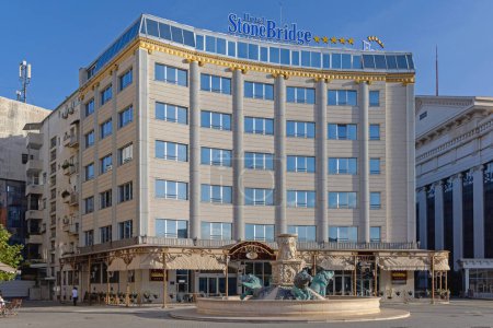 Foto de Skopje, Macedonia del Norte - 23 de octubre de 2023: Fuente de Leones frente al hotel de lujo de cinco estrellas Puente de piedra en el centro de la capital en el soleado día de otoño. - Imagen libre de derechos