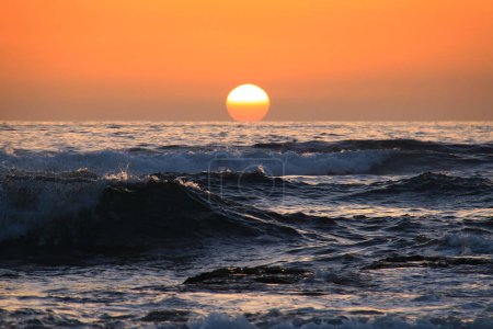 Téléchargez les photos : Le soleil dans un ciel orange qui se couche derrière les vagues de la mer. - en image libre de droit