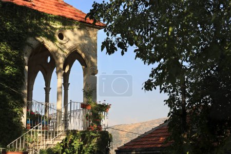 A traditional Lebanese house with arches from behind trees.