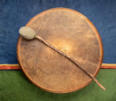 backlit, handmade, native American style, shaman frame drum covered by goat skin with a beater against colorful abstract paper landscape