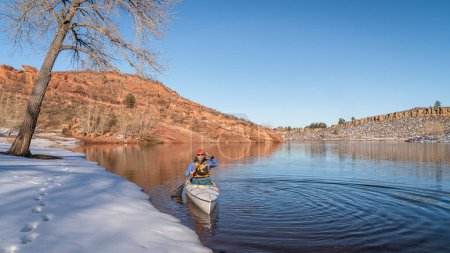 Téléchargez les photos : Senior male wearing life jacket is paddling expedition canoë in winter scenery of Horsetooth Reservoir in northern Colorado - en image libre de droit