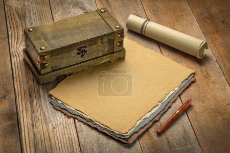 Photo for Sheets and roll of blank handmade paper with rough edges and a retro storage box against rustic weathered wood - Royalty Free Image