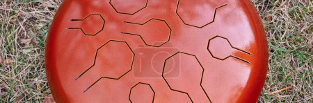 Photo for Red steel tongue drum on a ground covered by dry leaves, percussion instrument often used for meditation and sound therapy, panoramic web banner - Royalty Free Image