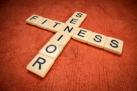 Foto de Crucigrama de fitness senior con azulejos de letras de marfil en papel naranja texturizado, concepto de salud y estilo de vida - Imagen libre de derechos