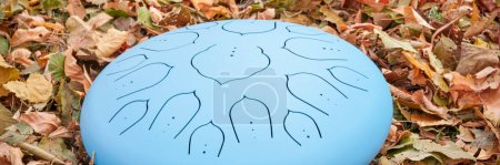 Photo for Blue steel tongue drum on a ground covered by dry leaves, percussion instrument often used for meditation and sound therapy - Royalty Free Image