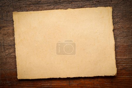 Téléchargez les photos : Feuille de papier blanc fait à la main avec des bords rugueux contre le bois rustique altéré - en image libre de droit