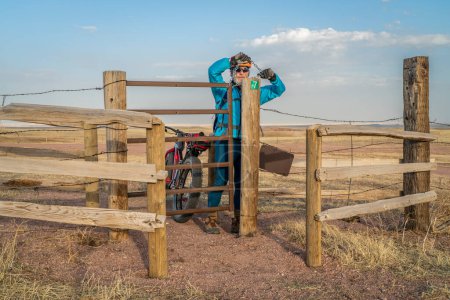 Photo for Biking in Soapstone Prairie Natural Area near Fort Collins, senior male cyclist with a fat mountain bike is closing a gate in a cattle fence - Royalty Free Image