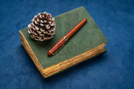 Photo for Retro leather-bound journal with decked edge handmade paper pages, decorative frosty pine cone and a stylish pen, journaling and winter holidays concept - Royalty Free Image