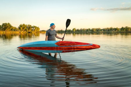 Photo for Senior male paddler with a long and narrow racing stand up paddleboard on a calm lake at sunset. - Royalty Free Image