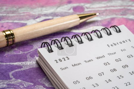 Téléchargez les photos : Février 2023 - petit calendrier de bureau en spirale avec un stylo élégant contre le papier marbré coloré, le temps et le concept d'entreprise - en image libre de droit