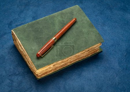 Photo for Retro leather-bound journal with decked edge handmade paper pages and a stylish pen on a textured blue bark paper, journaling concept - Royalty Free Image