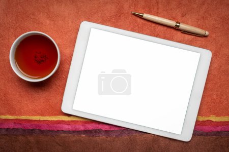 Téléchargez les photos : Maquette de tablette numérique avec écran isolé vierge (chemin de coupe inclus), couché à plat avec une tasse de thé contre un paysage abstrait en papier - en image libre de droit
