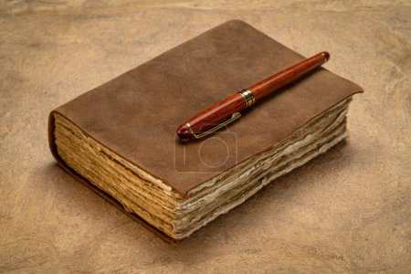 Foto de Retro leather-bound journal with decked edge handmade paper pages and a stylish pen on a textured bark paper, journaling concept - Imagen libre de derechos