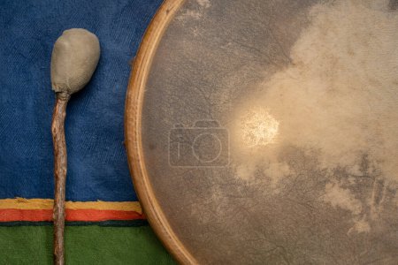 Foto de Retroiluminado, hecho a mano, estilo americano nativo, tambor de marco chamán cubierto por piel de cabra con un batidor contra el paisaje de papel abstracto colorido - Imagen libre de derechos