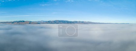 Foto de Dense fog covering foothills of northern Colorado with cler mountains at a horizon, aerial view of winter morning - Imagen libre de derechos