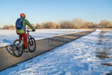 Téléchargez les photos : Male cyclist on a bike trail in winter scenery - Poudre River Trail in northern Colorado, biking, recreation and commuting concept - en image libre de droit