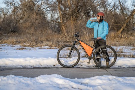 Photo for Senior cyclist with a mountain bike is taking a rest stop on Poudre River Trail near Greeley, Colorado, in winter scenery - Royalty Free Image