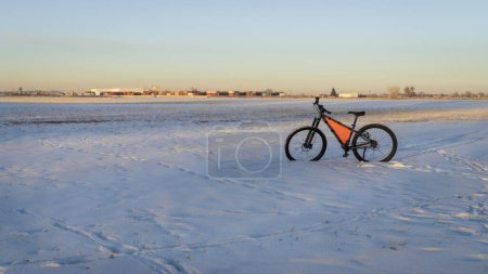 Téléchargez les photos : Mountain bike at winter sunset on a field covered by snow with industrial area in background - en image libre de droit