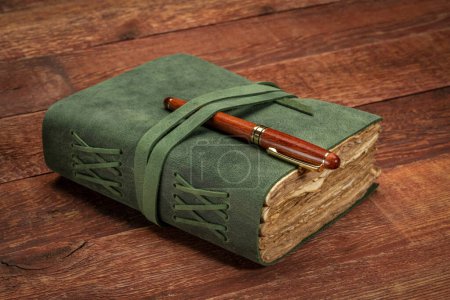 Foto de Retro leather-bound journal with decked edge handmade paper pages with a stylish pen on a rustic barn wood table, journaling concept - Imagen libre de derechos