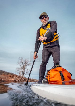 Téléchargez les photos : Senior paddler in a wet suit and life jacket is training on stand up paddleboard on a mountain lake in winter conditions - Horsetooth Reservoir in Colorado, POV from an action camera - en image libre de droit