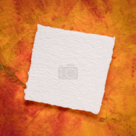 Foto de Pequeña hoja cuadrada de papel blanco Khadi en blanco contra papel de mármol colorido - Imagen libre de derechos