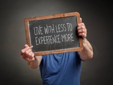 Foto de Live less to experience more, minimalism and lifestyle concept, white chalk handwriting on a blackboard held by a person - Imagen libre de derechos