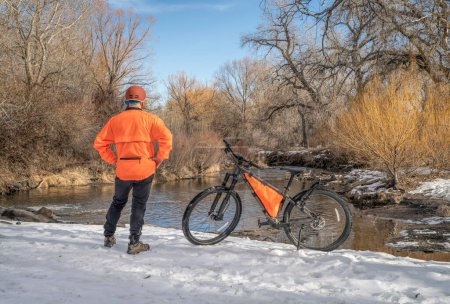 Foto de Ciclista varón maduro con una bicicleta de montaña en una orilla del río en el paisaje de invierno - Big Thompson River en Loveland, Colorado - Imagen libre de derechos