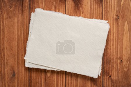 Téléchargez les photos : Small sheet of blank white Khadi rag paper against rustic wood background - en image libre de droit