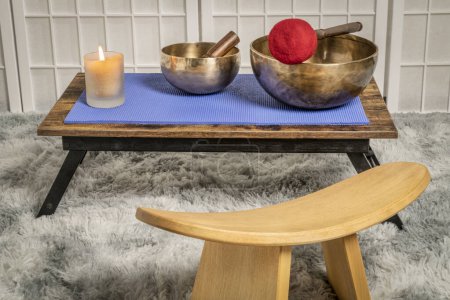 Téléchargez les photos : Large Tibetan singing bowl with a mallet, roller and wax candle on a low table, and kneeling bench, sound healing and meditation concept - en image libre de droit